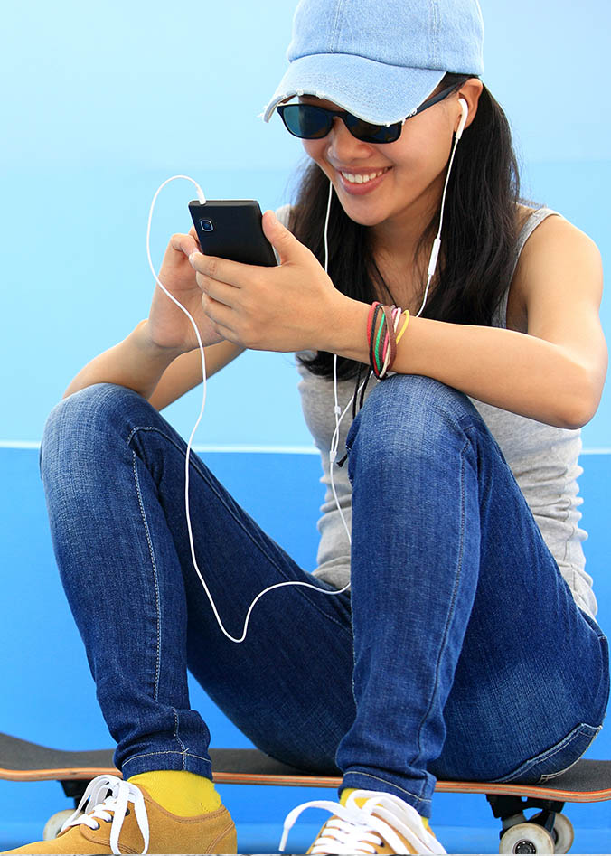 Credit Union Spending Controls and Alerts woman sitting on skateboard with earbuds in typing on her phone
