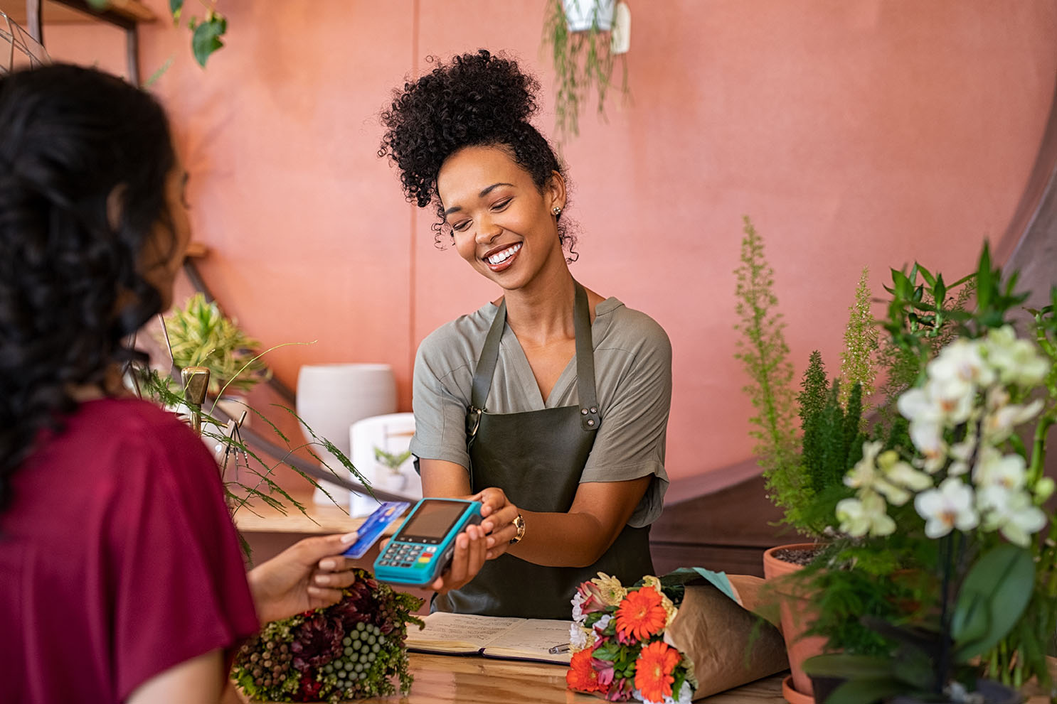 Smiling,Florist,Holding,Card,Reader,Machine,At,Counter,With,Customer