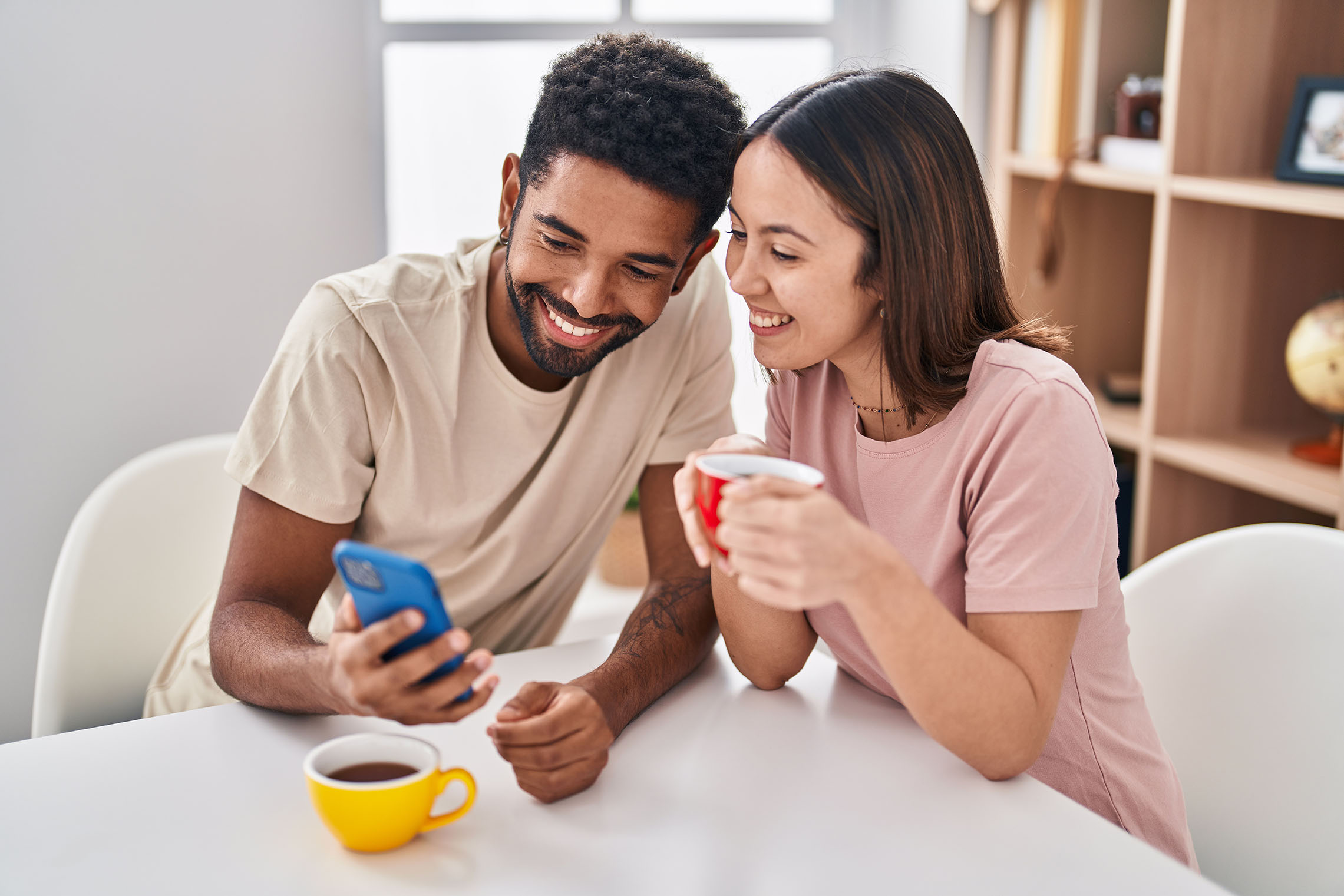 Man,And,Woman,Couple,Sitting,On,Table,Drinking,Coffee,Using Man and woman couple sitting on table drinking coffee using smartphone at home