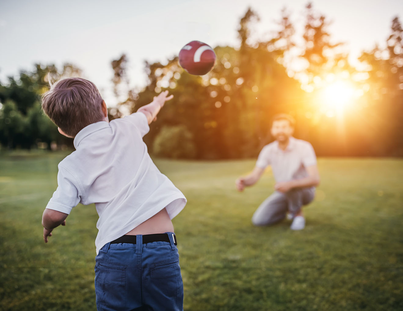 Dad and Son Playing Football Dad with his little cute son are having fun and playing American football on green grassy lawn